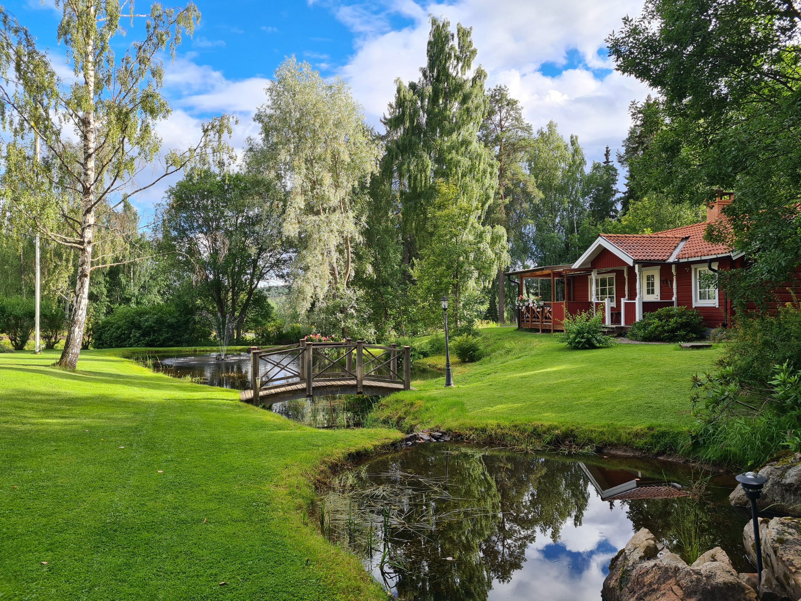 Stugan i Norsbo med de två dammarna framför en sommardag